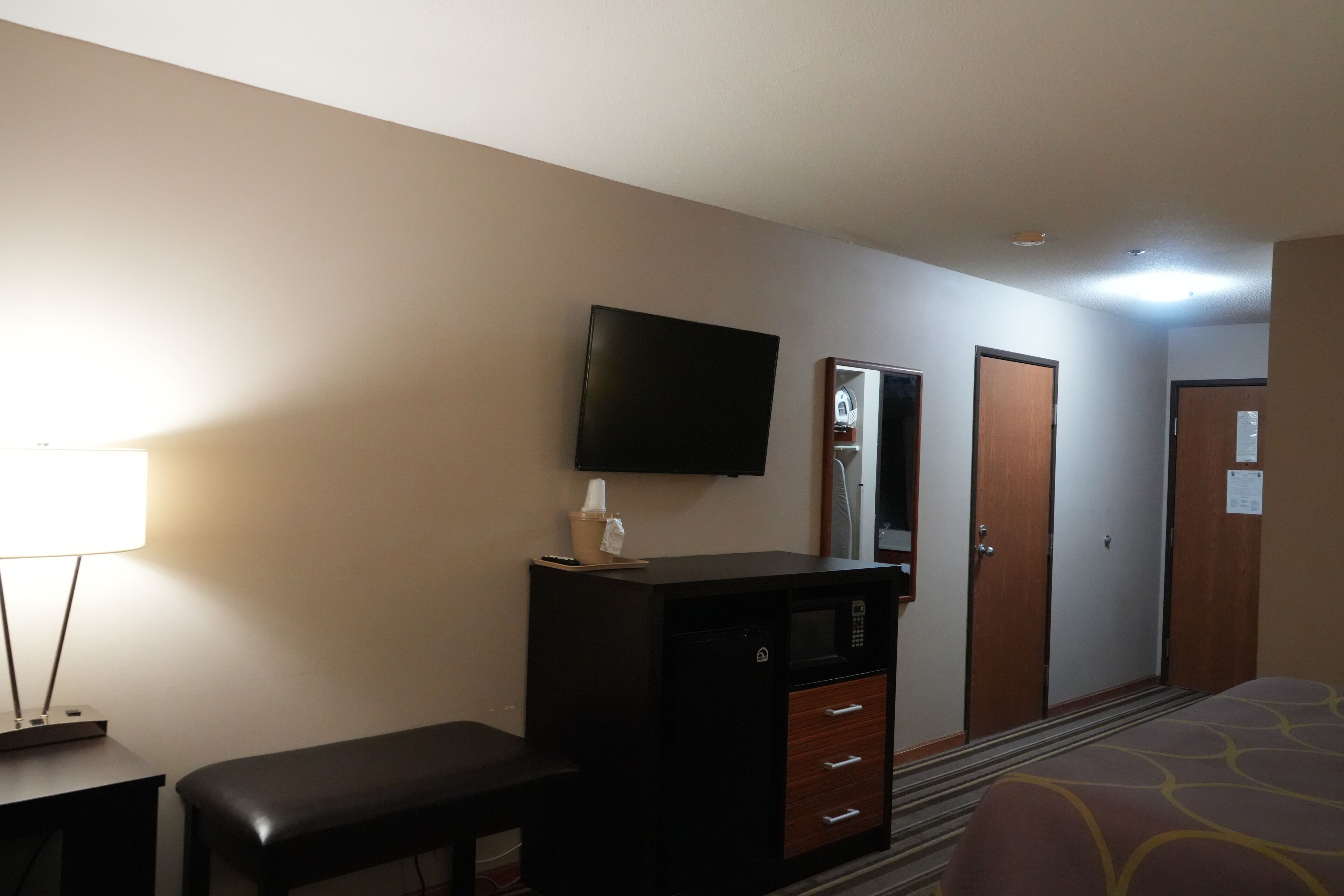 Ein Hotelzimmer mit einem Bett, einem Schreibtisch mit Lampe, einer Mikrowelle, einer Bank und einem Fernseher an der Wand.