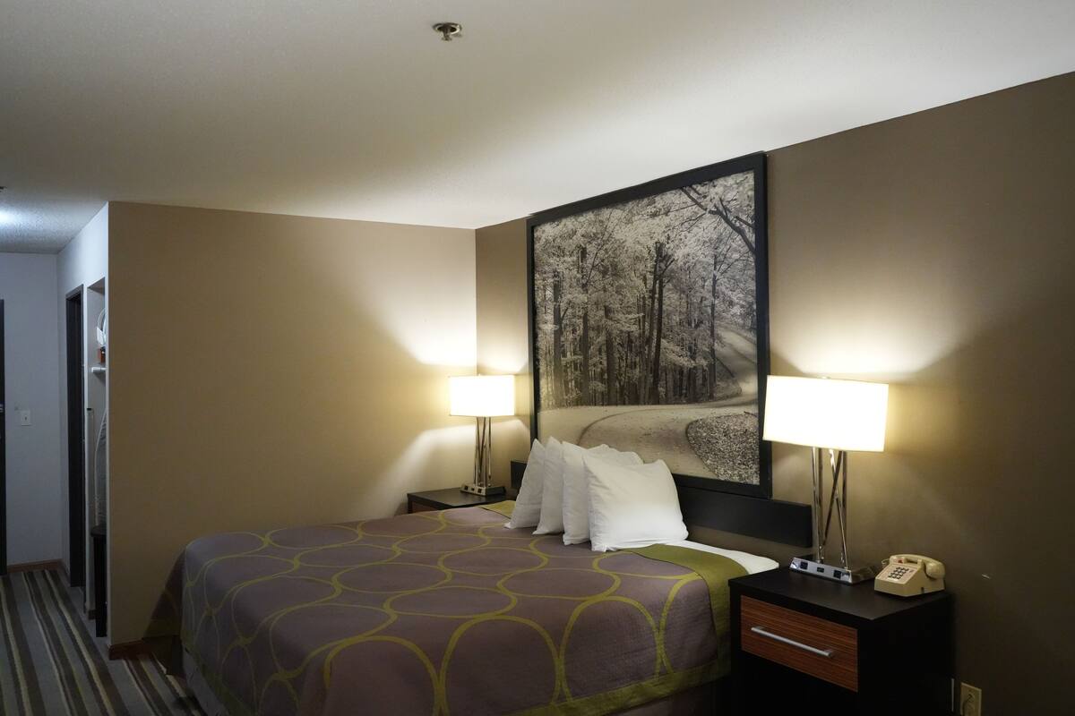 Habitación de hotel con una cama, dos lámparas de noche, una mesita de noche con un teléfono y un cuadro en la pared.