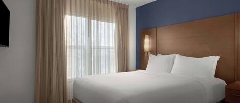 Una habitación de hotel con cama, cortinas, mesita de noche y lámpara de pared.