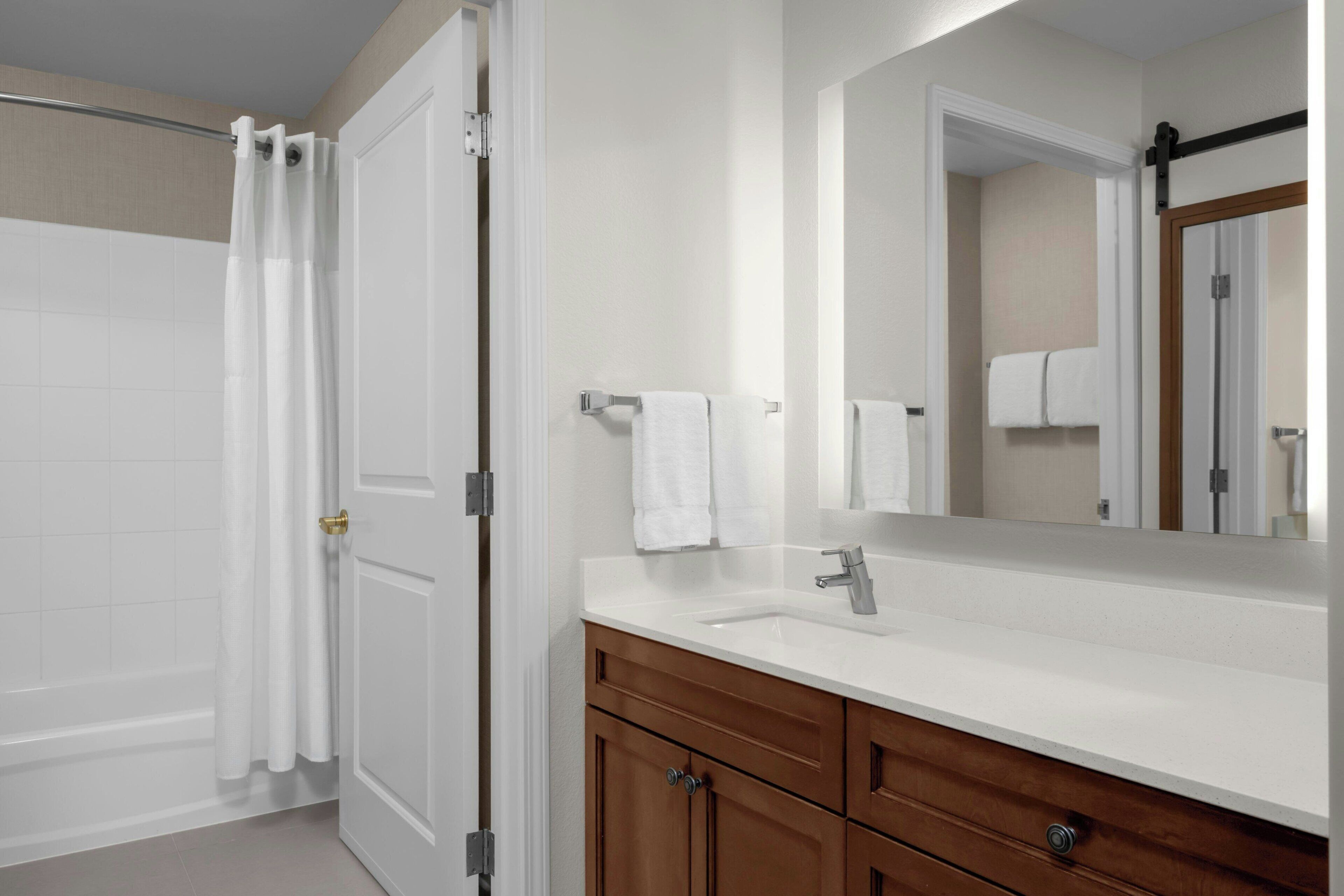 A bathroom with a white bathtub, a white sink, wooden cabinets, and a mirror.