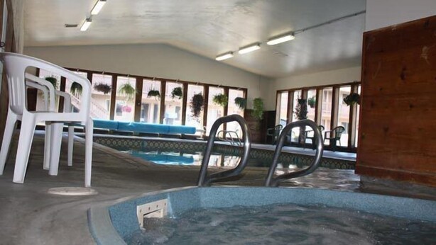 Une piscine intérieure avec un bord carrelé de bleu, des chaises en plastique blanches et des échelles métalliques pour accéder à la piscine.