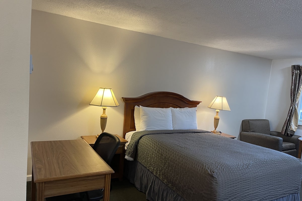 A hotel room with a bed, two bedside tables with lamps, a wooden desk, and a chair.