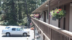 Un motel doté d’un espace extérieur abrité, d’une voiture blanche garée devant et de jardinières suspendues.