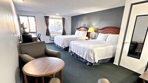Une chambre d’hôtel avec deux lits, une table ronde et deux fauteuils.