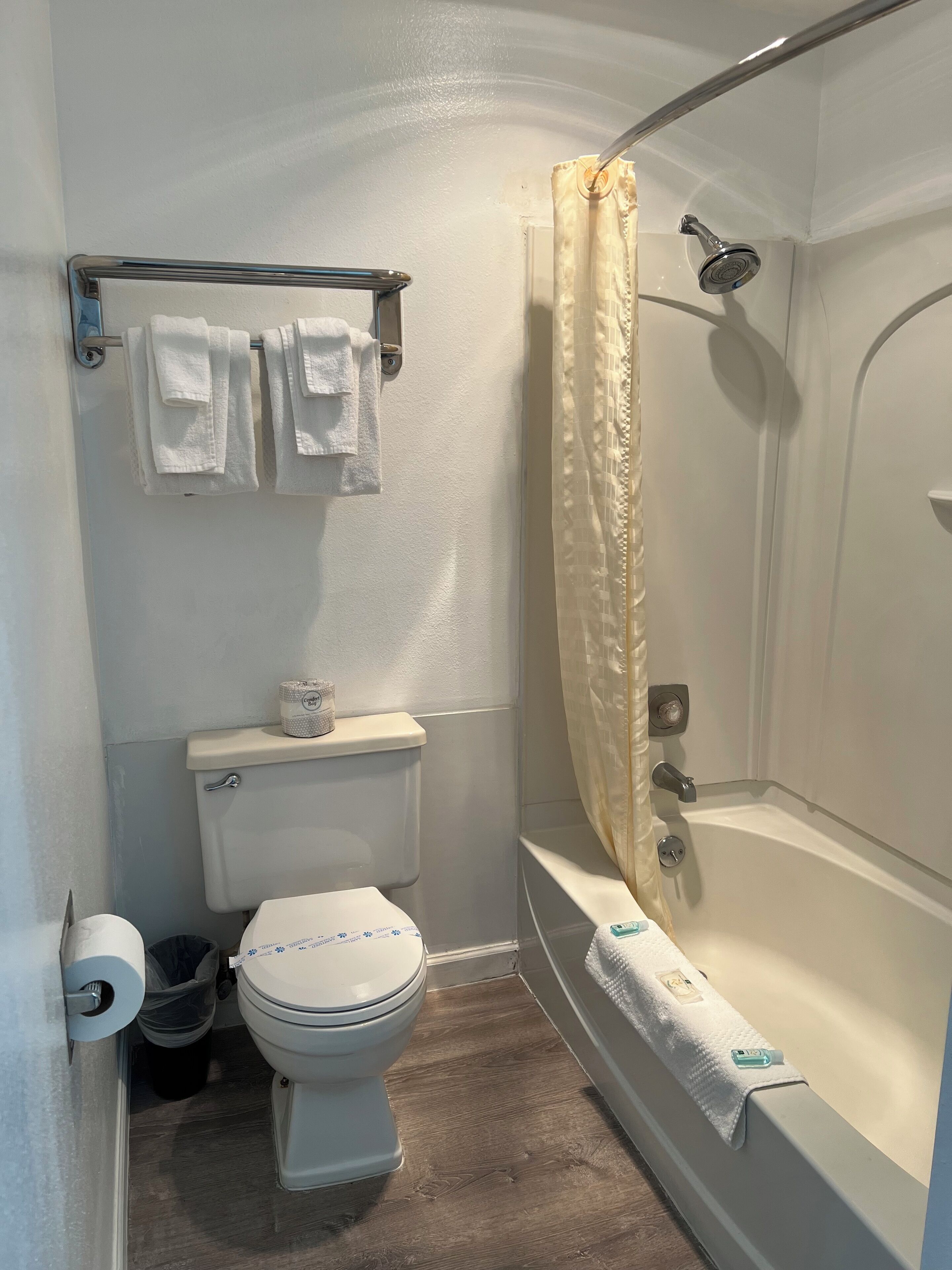 Un baño pequeño con inodoro, ducha con cortina y un perchero con toallas.