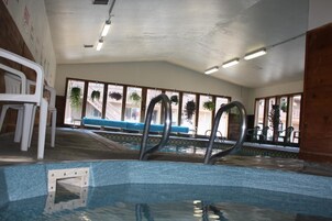 Una piscina interior con agua cristalina, zona junto a la piscina en tonos azules y vista a un edificio a través de amplias ventanas.