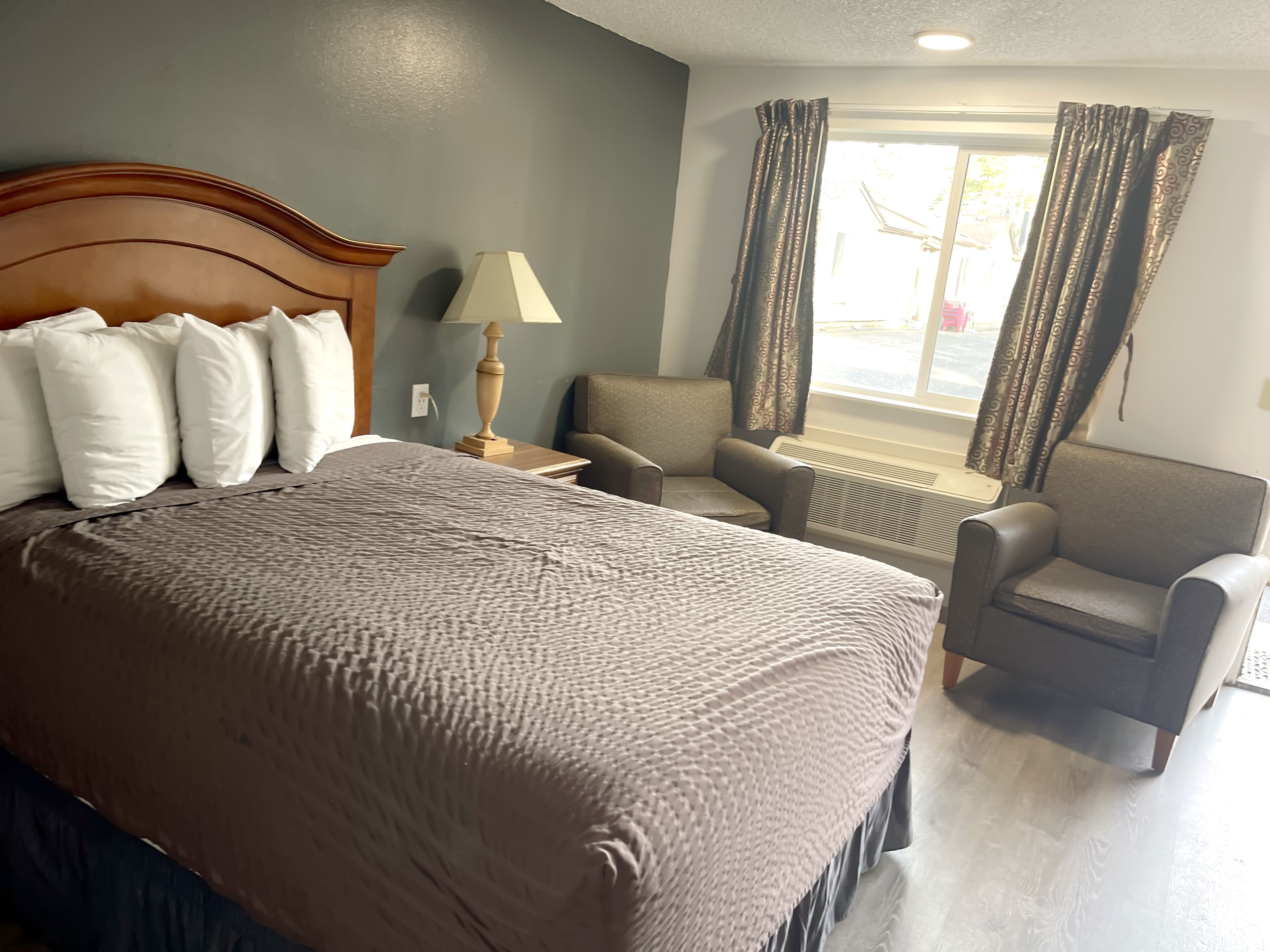 A hotel room with a large bed, a chair, a lamp, and a window with curtains.
