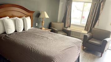 A hotel room with a large bed, a chair, a lamp, and a window with curtains.