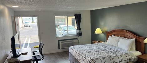 Une chambre d’hôtel équipée d’un lit, d’un bureau, d’une chaise et d’une fenêtre donnant sur un parking.