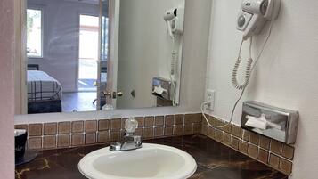 Uma casa de banho com uma pia branca, um espelho, um secador de cabelo e um dispensador de lenços.