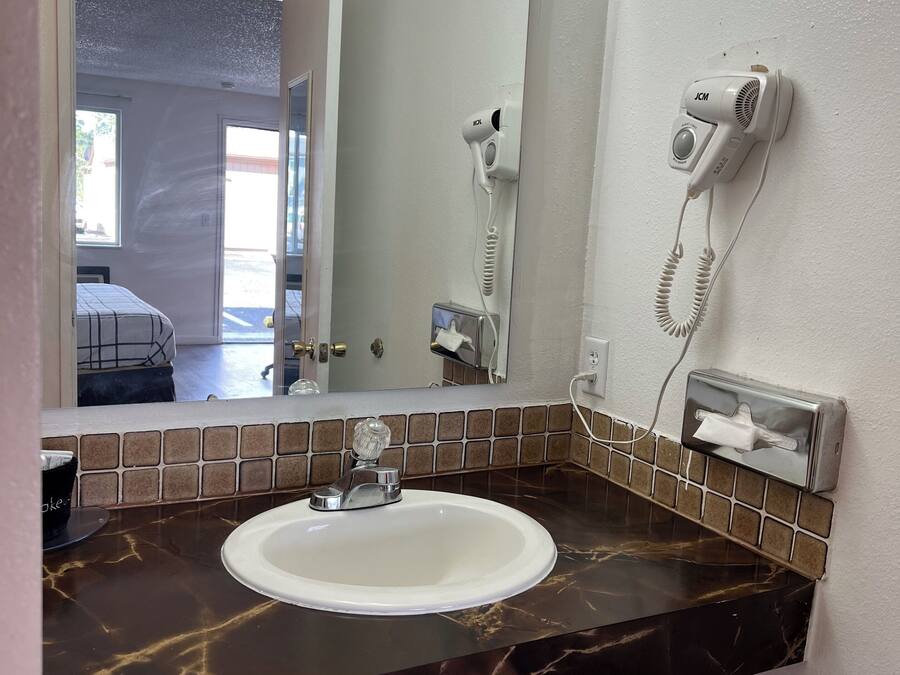 Uma casa de banho com uma pia branca, um espelho, um secador de cabelo e um dispensador de lenços.