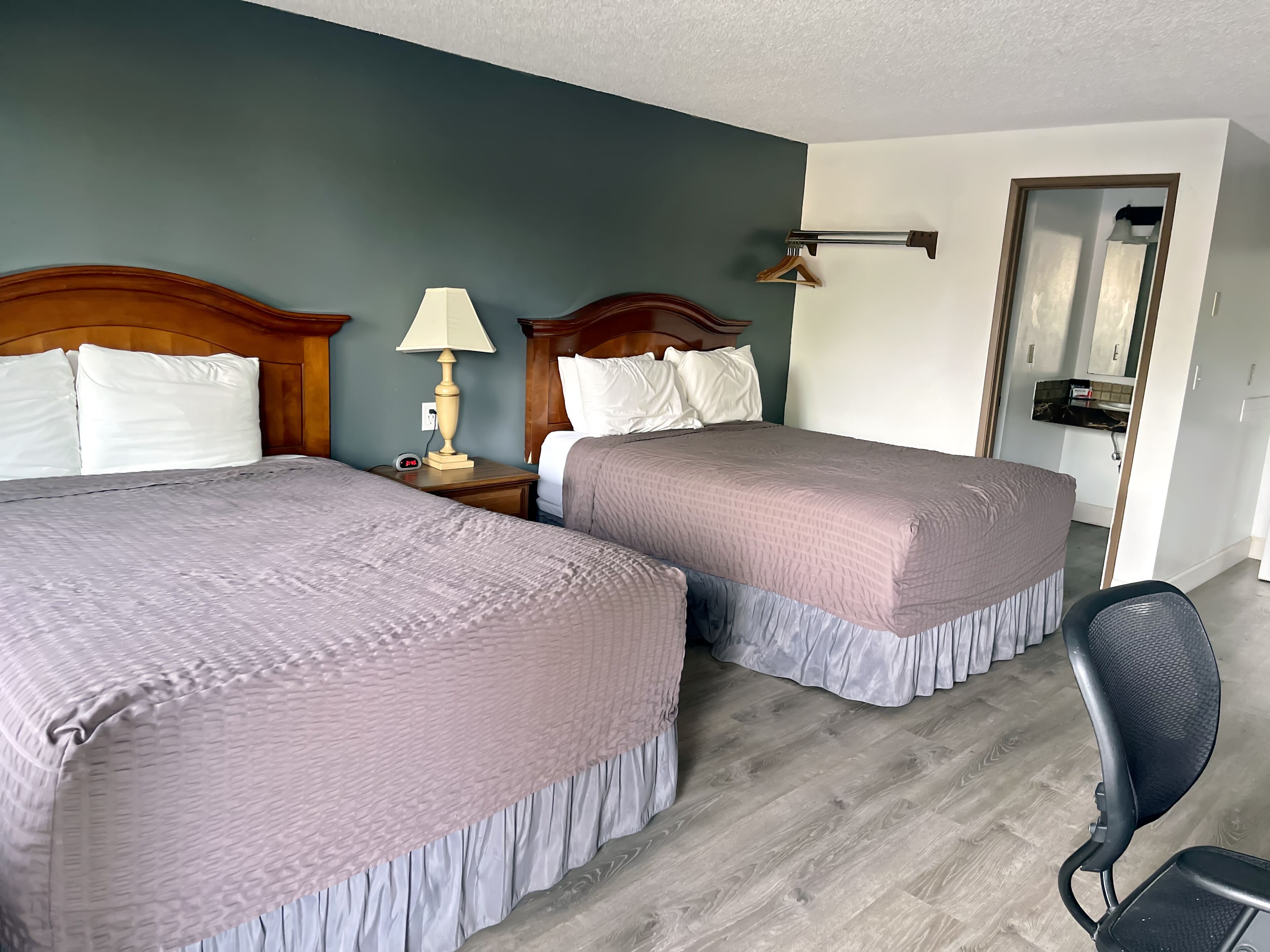 Une chambre d’hôtel avec deux lits, une table de chevet avec une lampe, une chaise et un miroir.