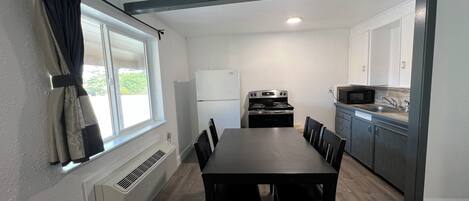 A compact kitchen with a dining table and chairs, a white refrigerator, a stove, and a microwave.