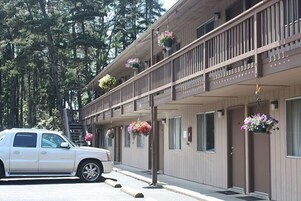Un motel de dos pisos, con varios balcones adornados con macetas colgantes y un coche estacionado al frente.