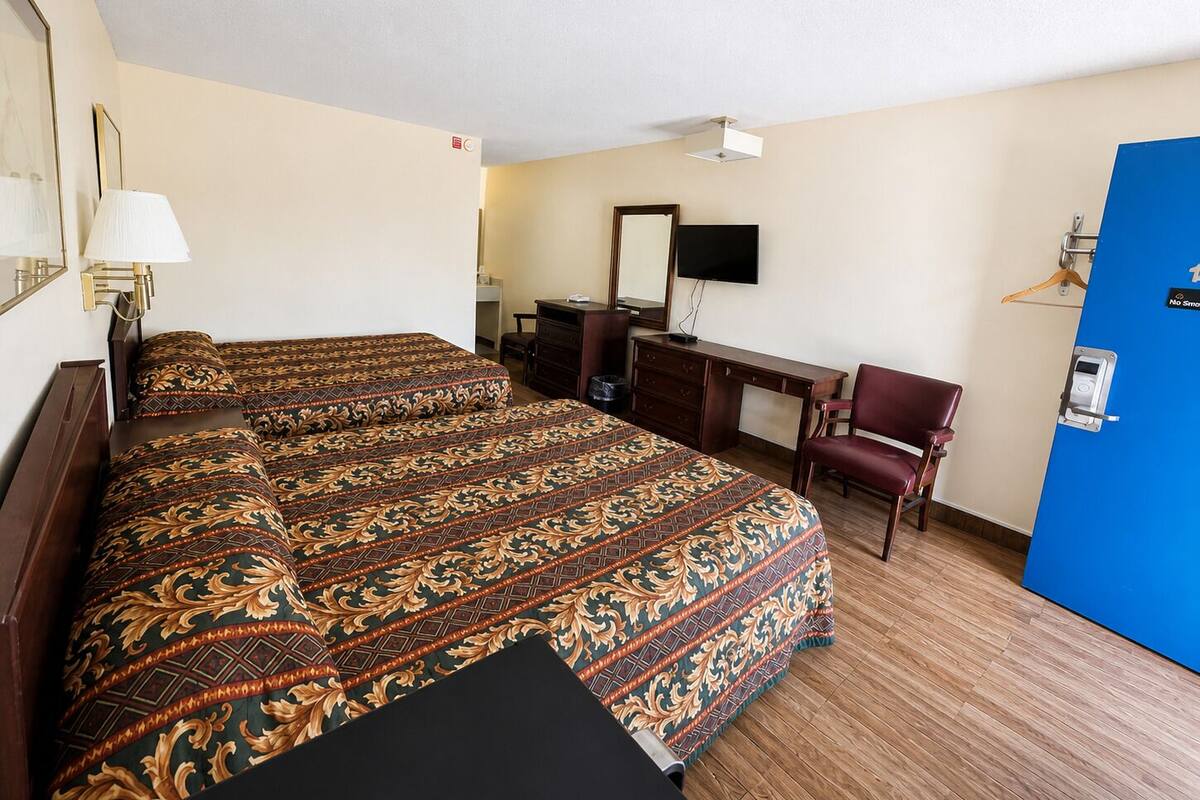 Ein Hotelzimmer mit zwei Betten, einem Schreibtisch, einem Stuhl, einem Fernseher und einer blauen Tür.