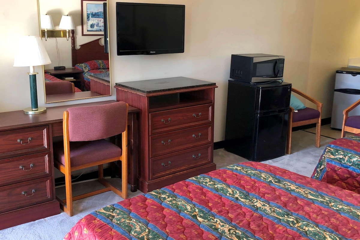 A hotel room with a bed, a desk with a lamp, a dresser, a television, a microwave, and a refrigerator.