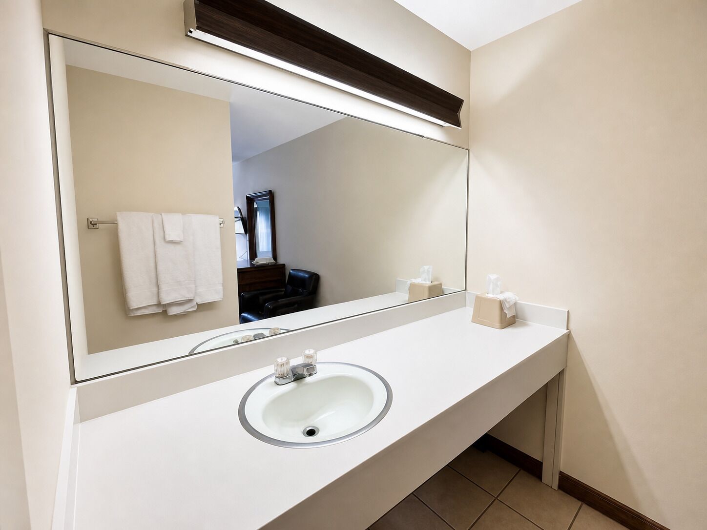 Un baño con un espejo grande, un lavamanos y un perchero para toallas.