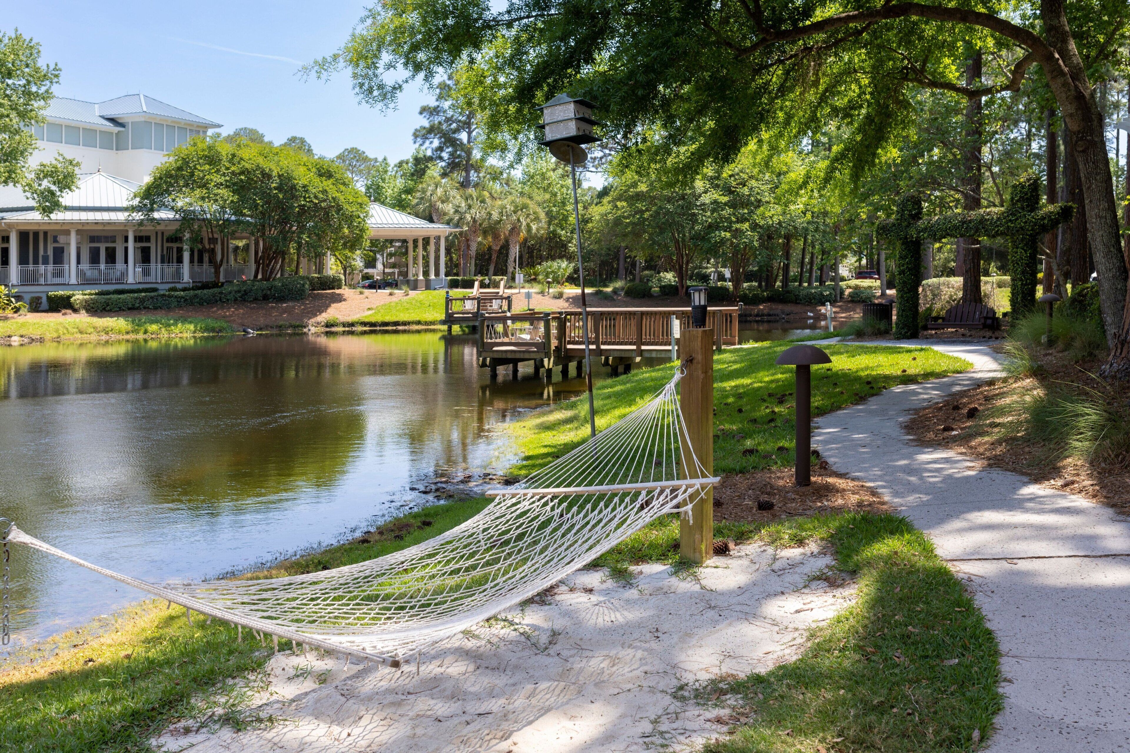 A hammock by a pond, wooden deck, and a gazebo in a park setting.