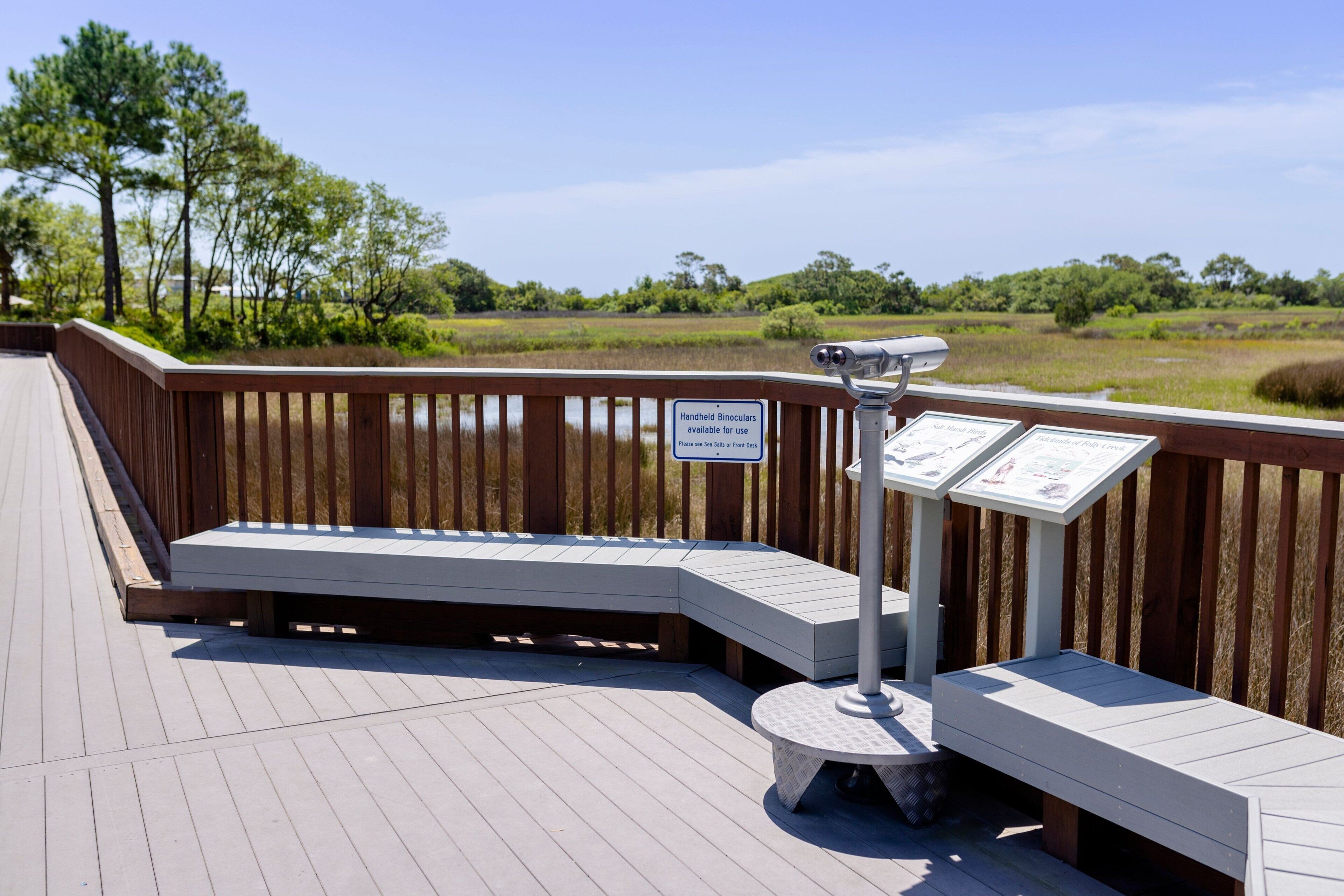 A wooden deck with a telescope and informational signs, overlooking a natural landscape.