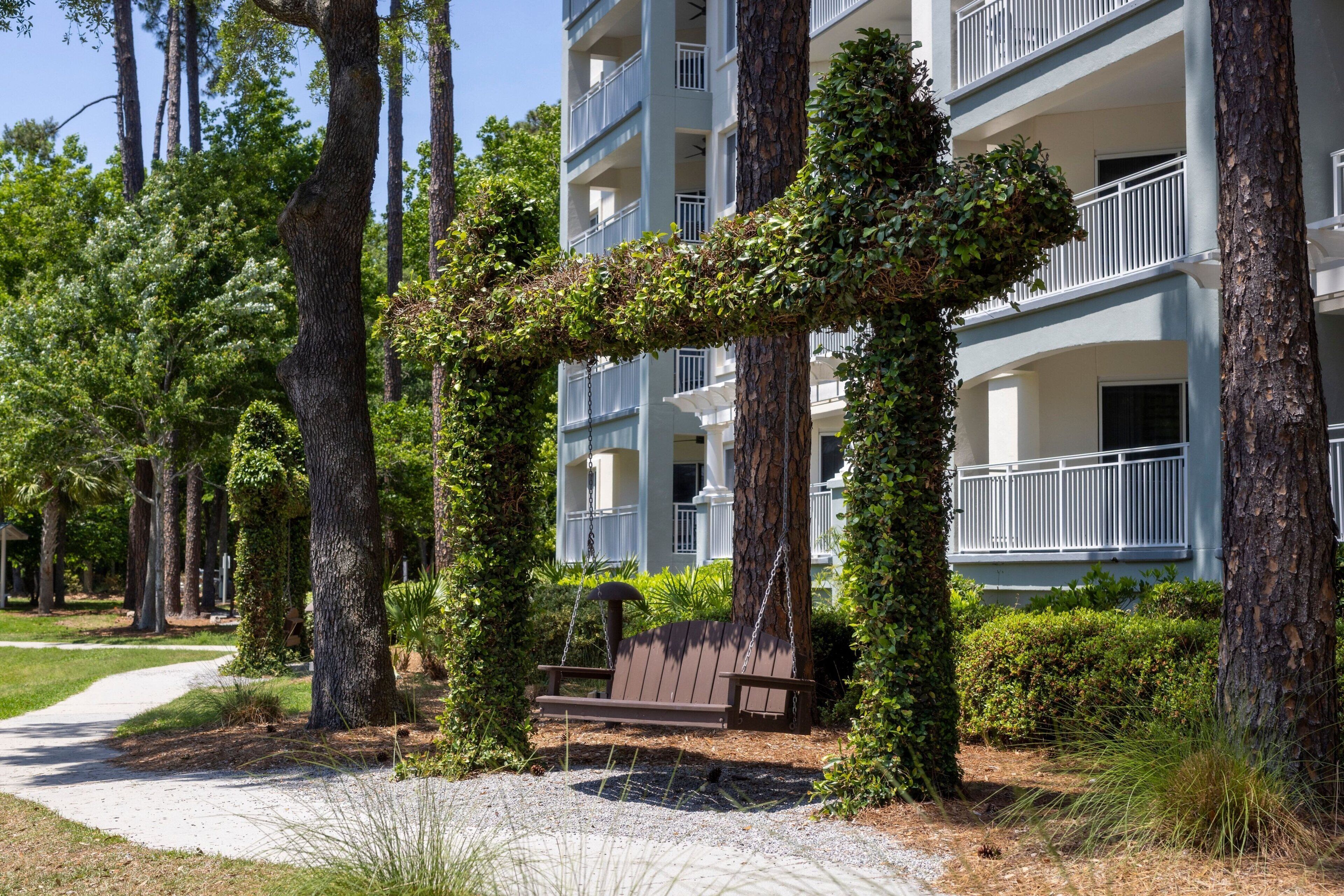 A building with multiple balconies, surrounded by trees and a pathway.