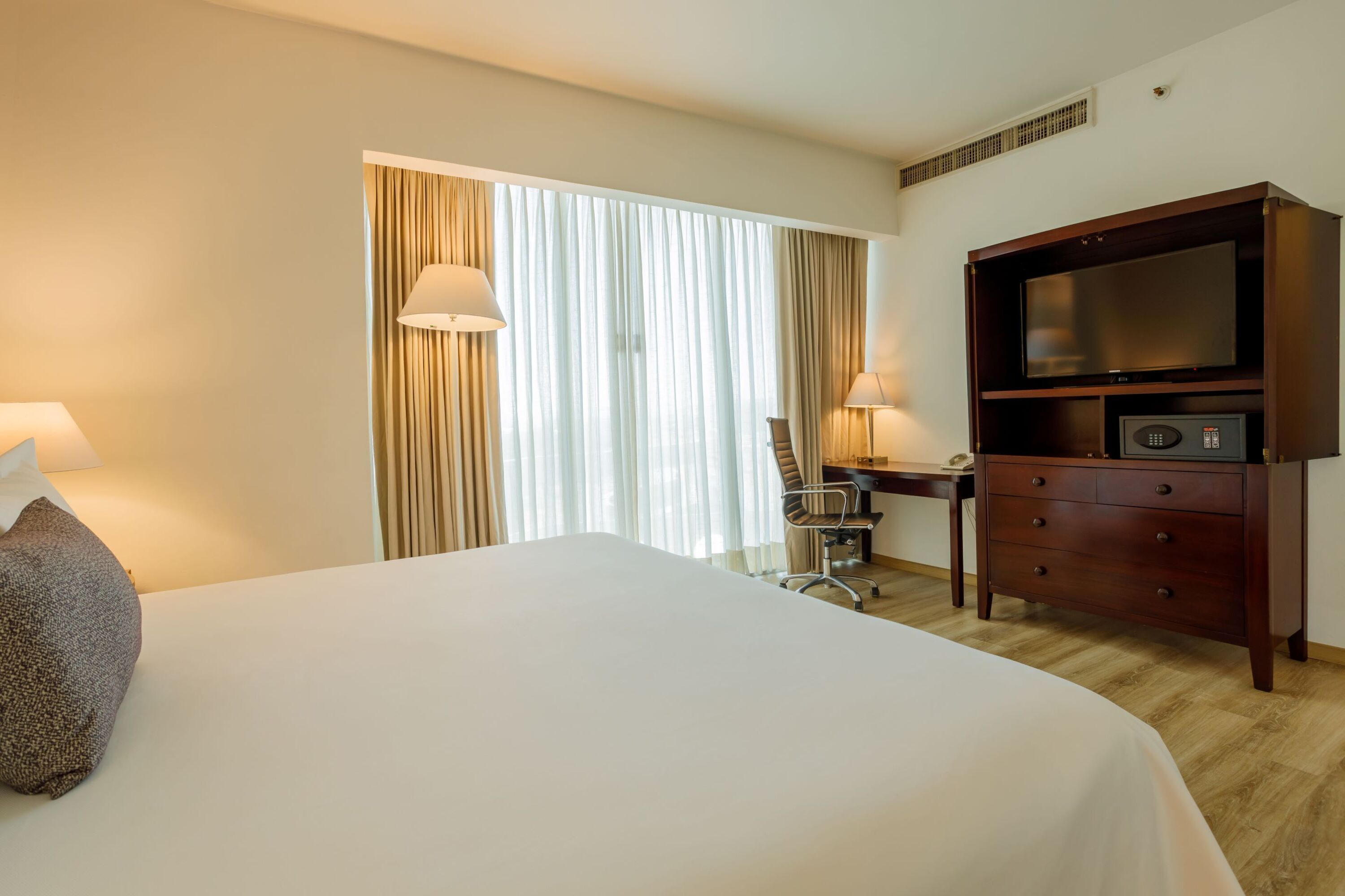 A hotel room with a large bed, a desk with a chair, a television, and a lamp.