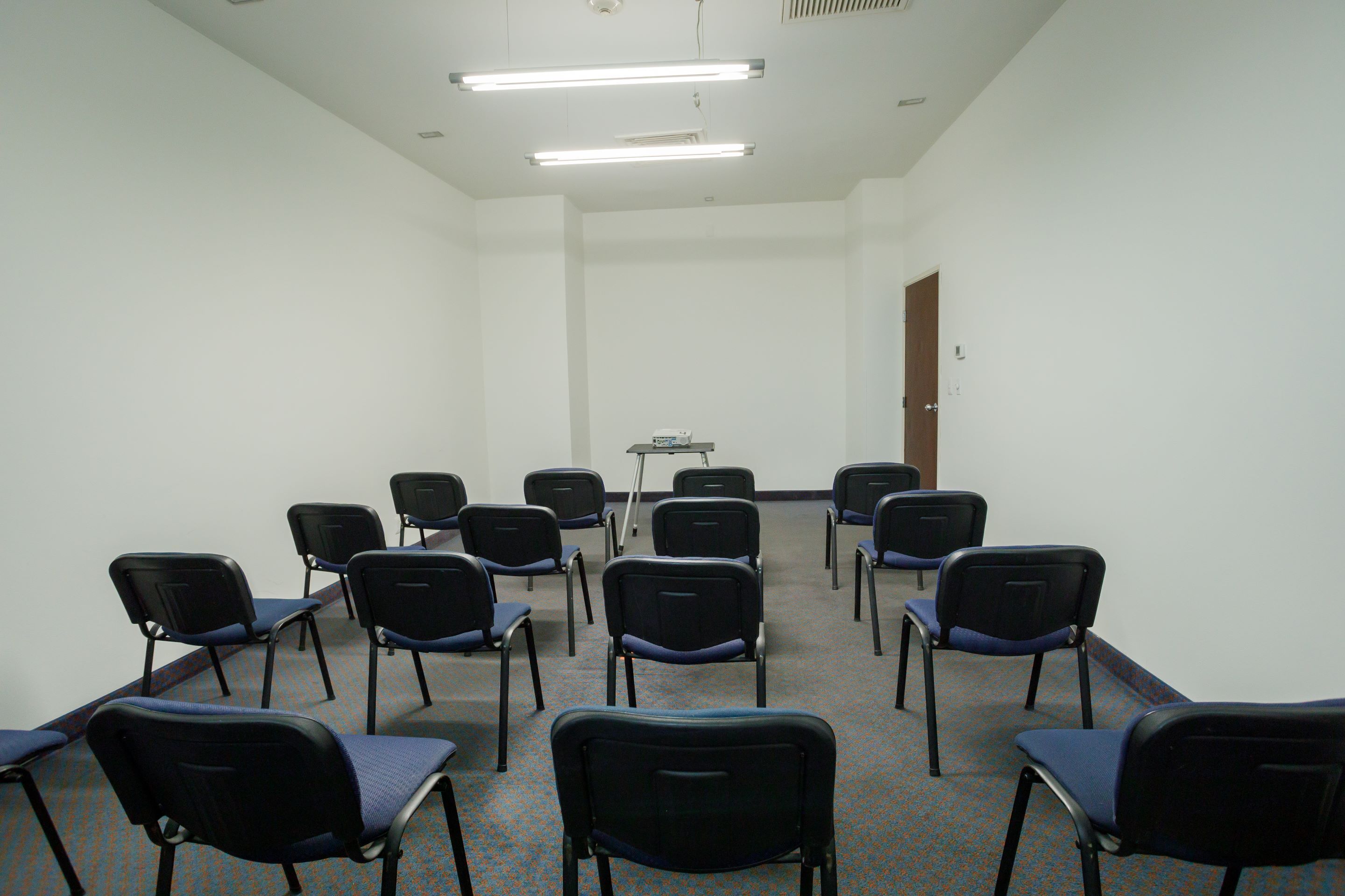 Une salle de conférence avec des rangées de chaises, un projecteur et un tableau blanc.