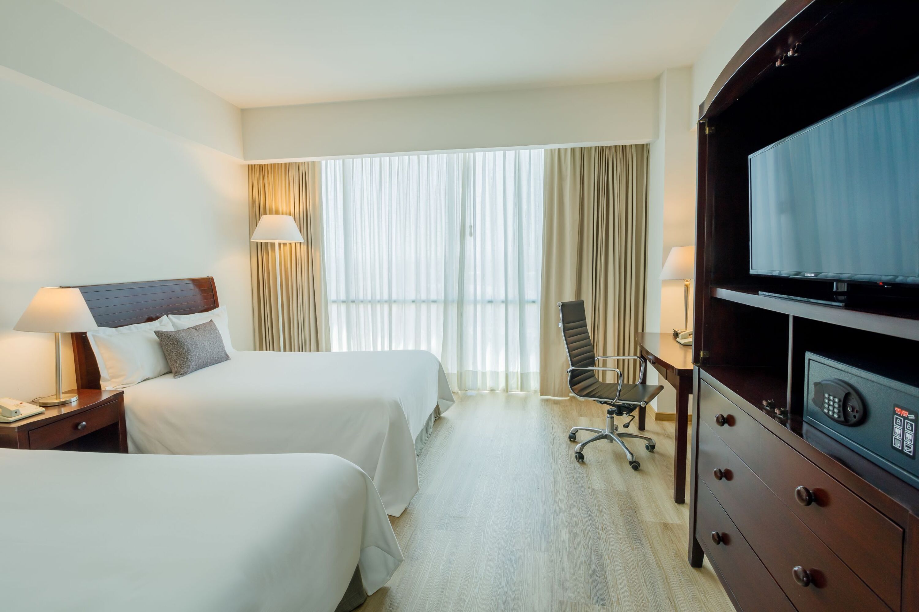 Ett hotellrum med två sängar, ett skrivbord, en stol, en TV och en minibar.