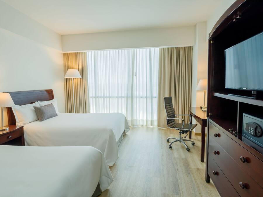 Ett hotellrum med två sängar, ett skrivbord, en stol, en TV och en minibar.