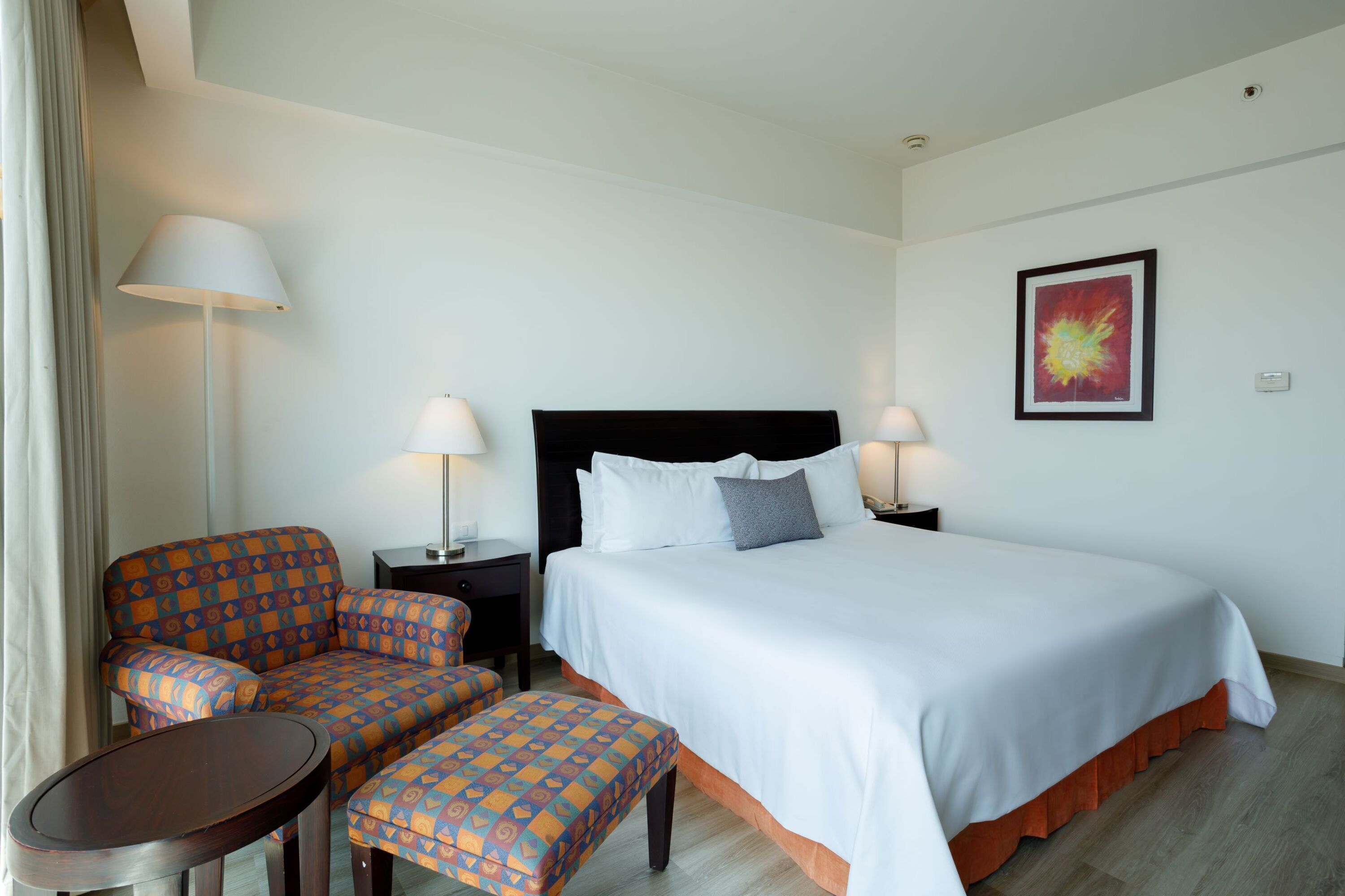 Habitación de hotel con cama, dos sillones, una mesita y dos lámparas de noche.