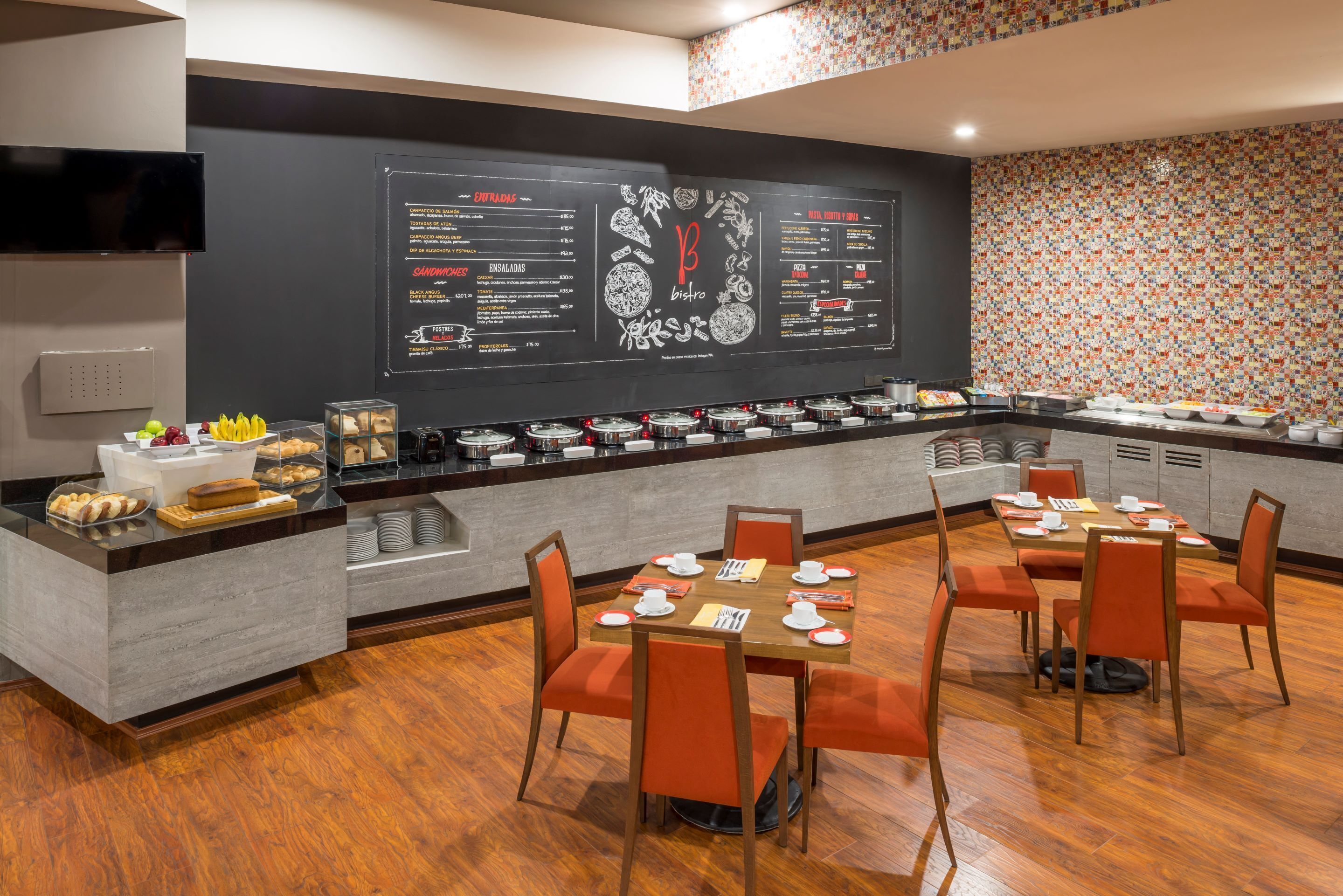 A modern restaurant with a black menu wall, wooden tables, and orange chairs.