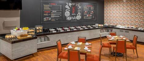 A modern restaurant with a black menu wall, wooden tables, and orange chairs.