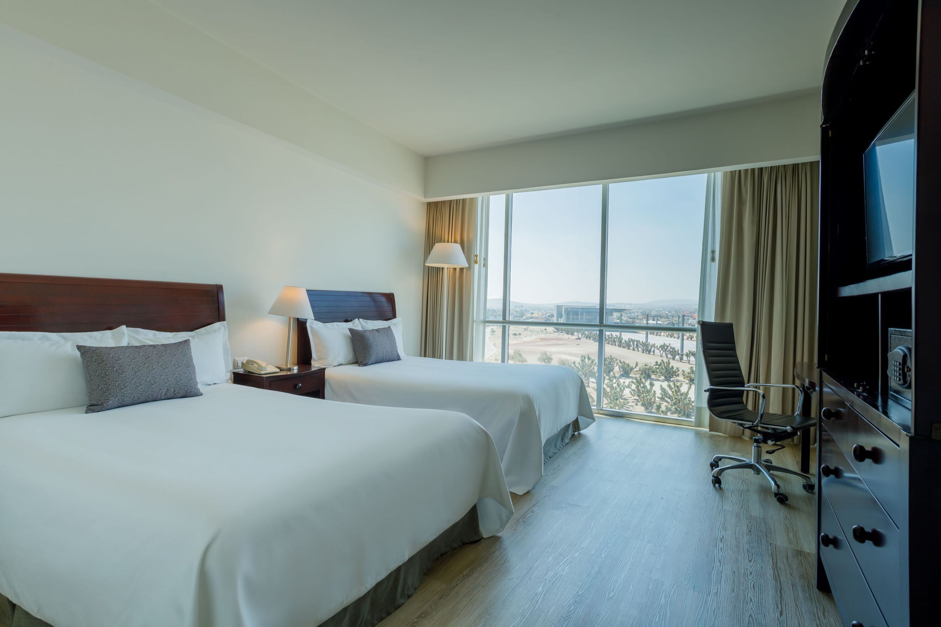A hotel room with two beds, a desk, a chair, and a TV.