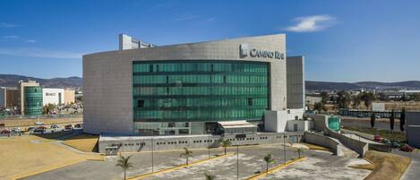A modern building with a large glass facade, a parking lot with yellow lines, and a clear sky.