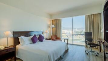 Habitación de hotel con una cama grande, dos mesitas de noche, un escritorio, una silla y vistas a la ciudad.