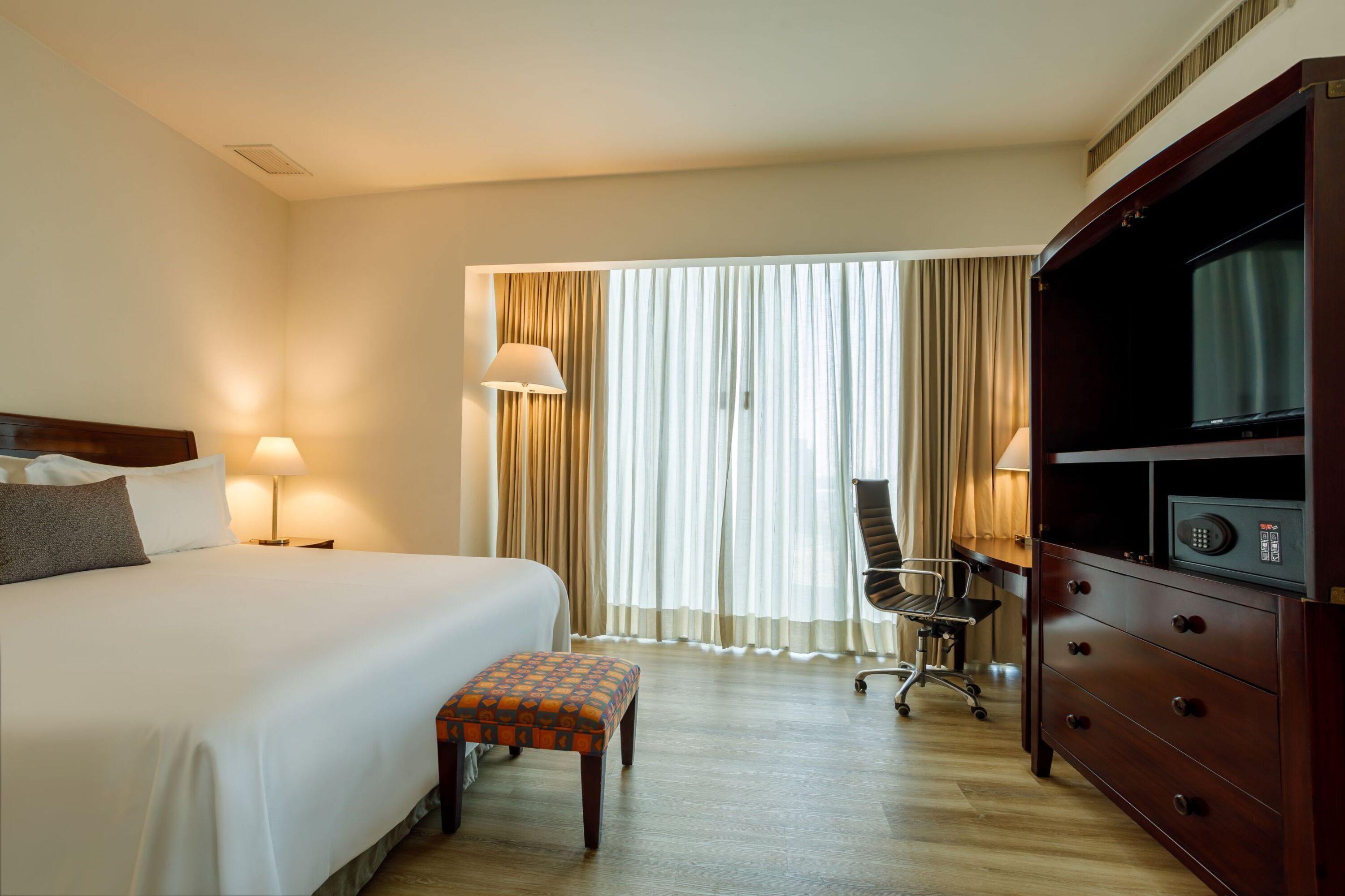Una habitación de hotel con una cama, un escritorio, una silla, un televisor y una caja fuerte.