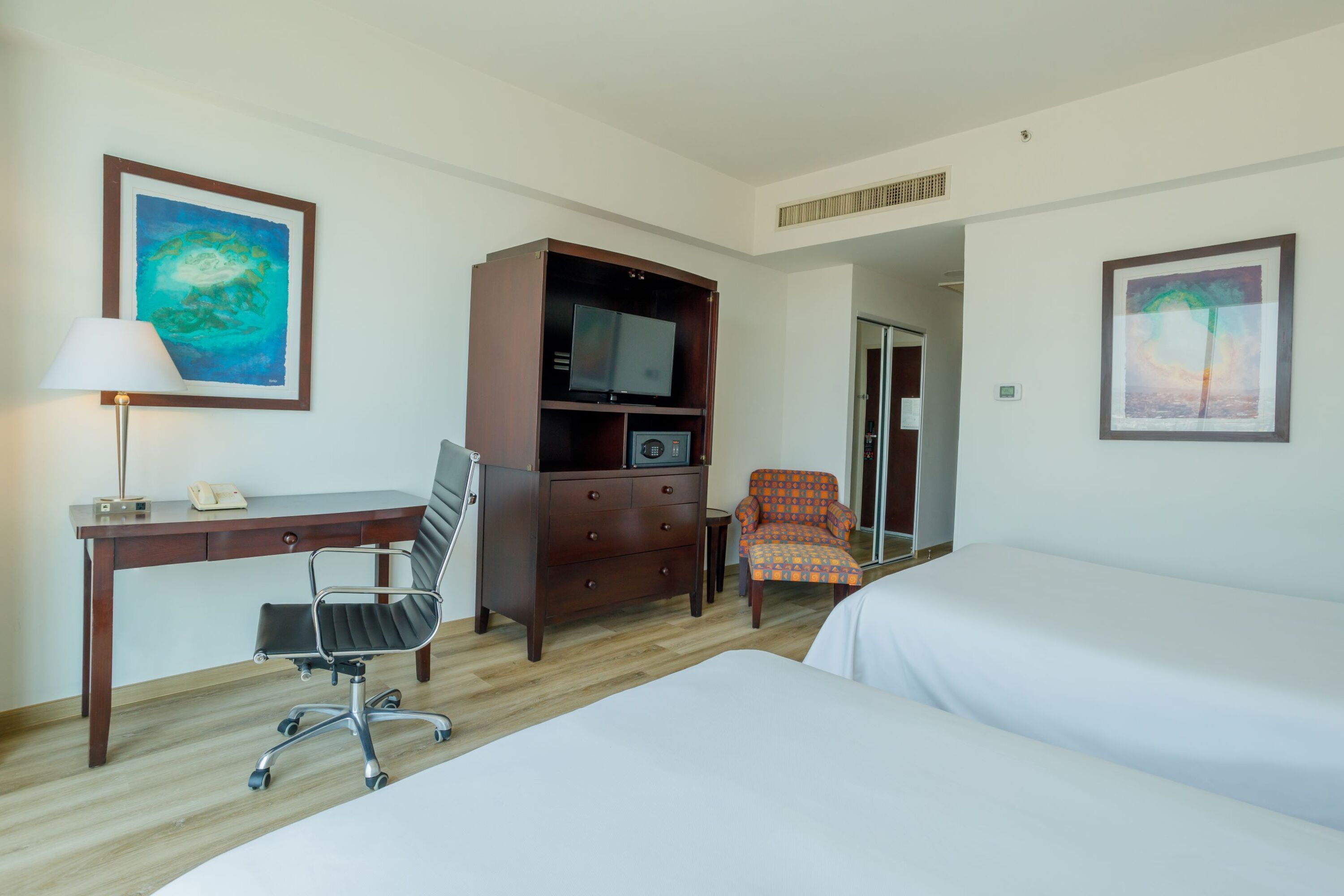 A hotel room with a desk, chair, TV, and two beds.
