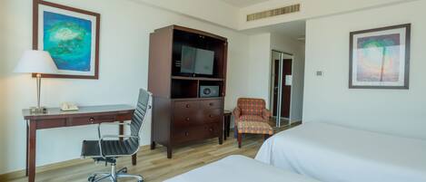 A hotel room with a desk, chair, TV, and two beds.