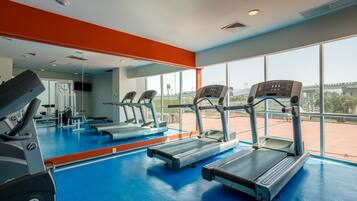 Un gimnasio con cintas de correr, un espejo grande y amplias ventanas con vistas al exterior.