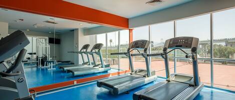 Une salle de sport équipée de tapis de course, dotée d’un mur recouvert de miroirs et de grandes fenêtres donnant sur l’extérieur.