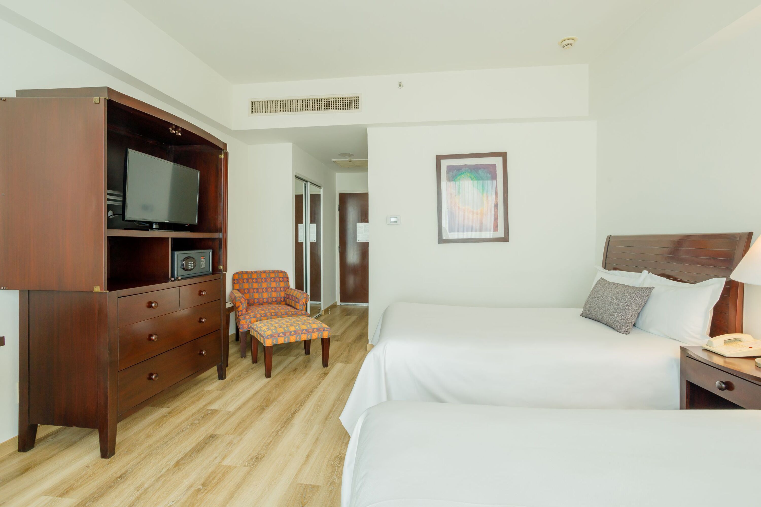 A hotel room with two beds, a wooden dresser with a television, a chair, and a framed picture on the wall.