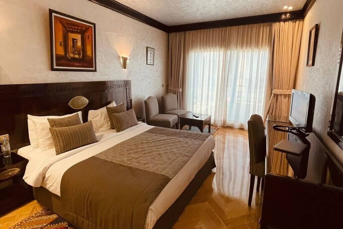 A hotel room with a large bed, a desk, a chair, a television, and a window with curtains.