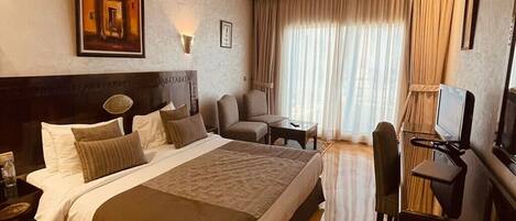 A hotel room with a large bed, a desk, a chair, a television, and a window with curtains.