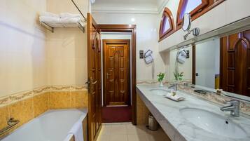 Une salle de bain avec une porte en bois, une baignoire blanche, un grand miroir et un lavabo avec des articles de toilette.