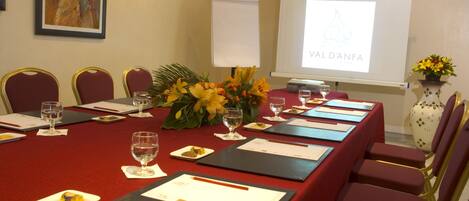 A conference room with a long table, red chairs, and a projector screen displaying "VALD'ANFA".