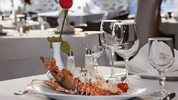 Una mesa de comedor con un plato de langosta, saleros, posavasos para copas de vino y una rosa.