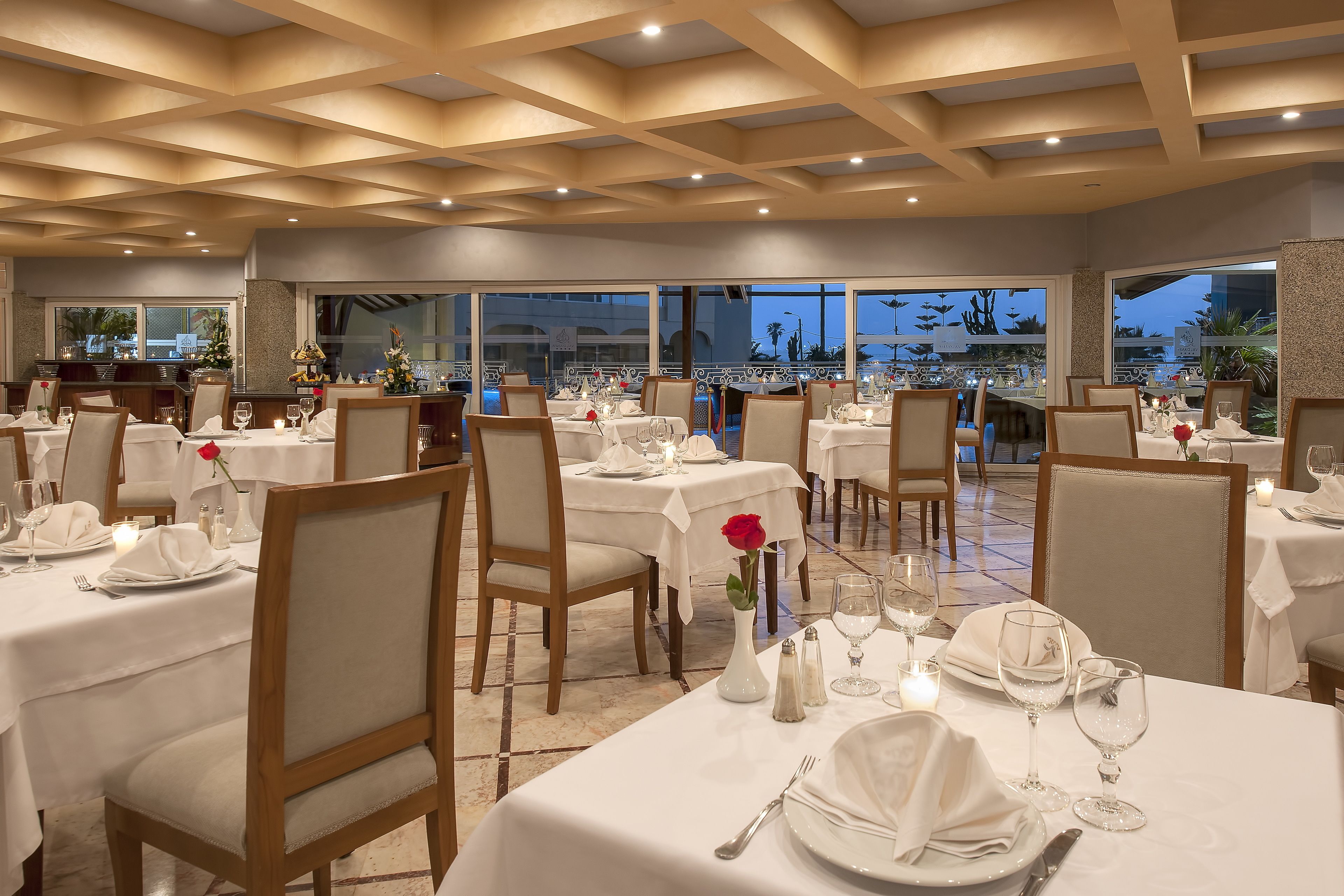 A restaurant with multiple tables set for dining, featuring white tablecloths, chairs, and candles.