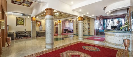 Um hall amplo com pé direito alto, colunas ornamentadas e tapete vermelho.