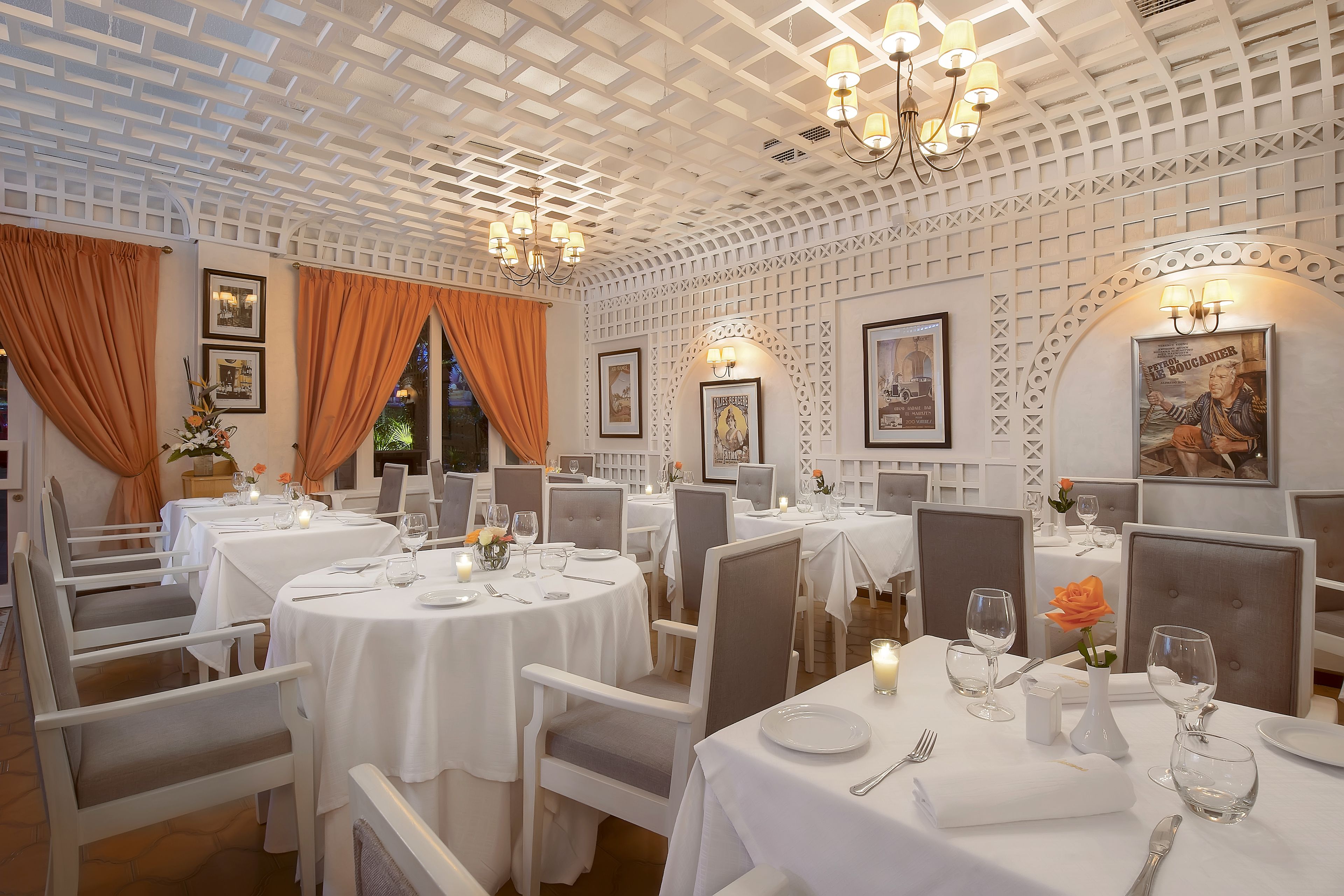 A restaurant with round tables, white tablecloths, and grey chairs.