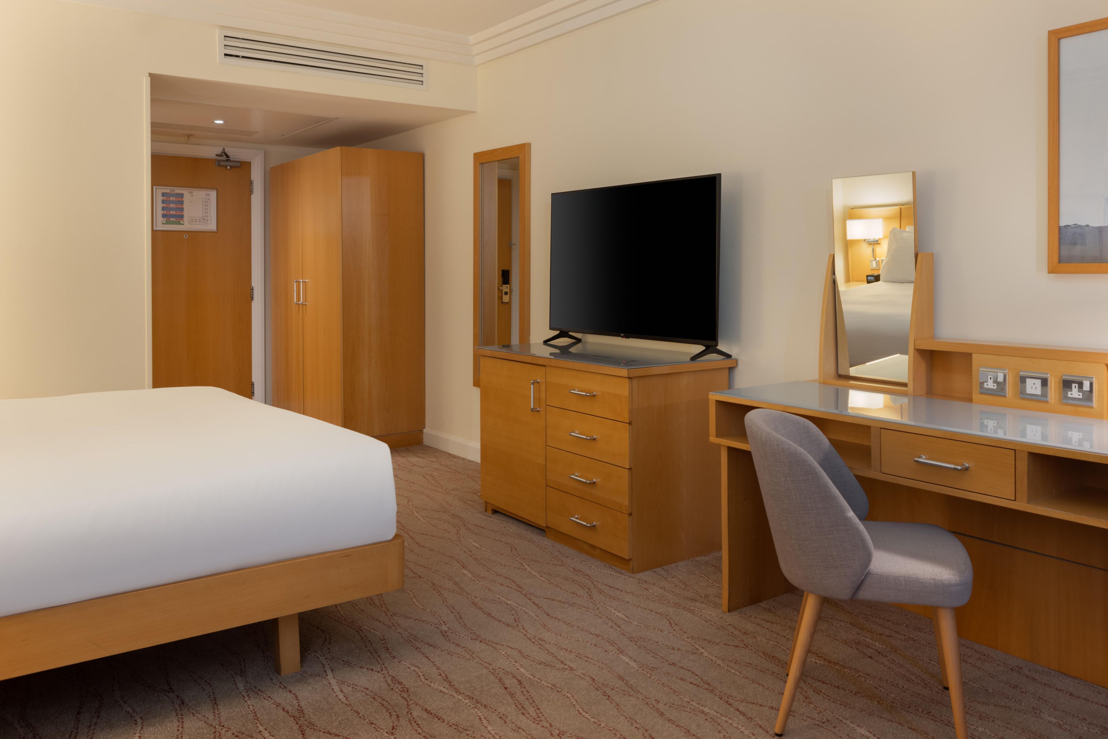 Habitación de hotel con cama, escritorio con silla, televisor, armario y espejo.