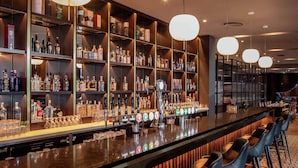 Een bar met drankflessen op planken, een bar en krukken, en hanglampen.